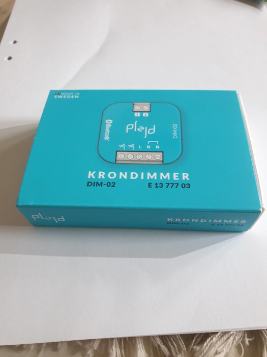 Ny Plejd krontimmer DIM-02 i blå förpackning på ett vitt bord.