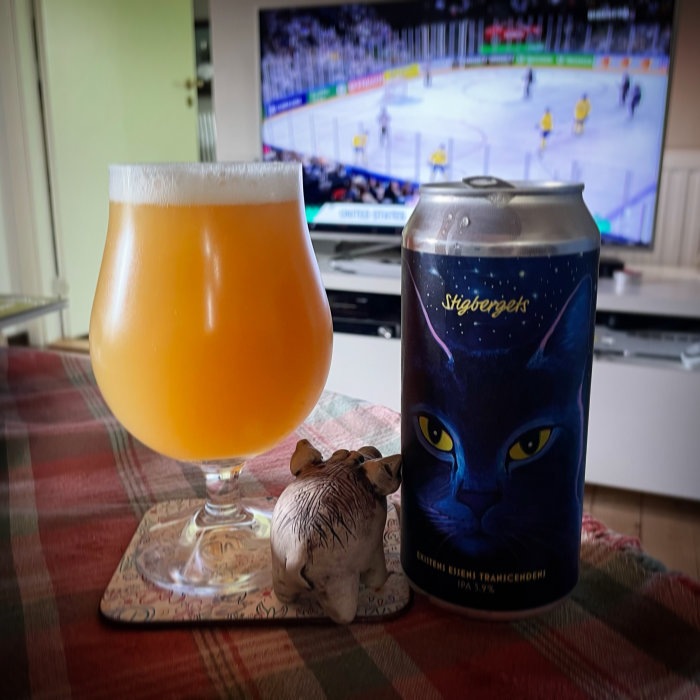 Ölglas och ölburk med kattmotiv framför tv som visar en hockeymatch.