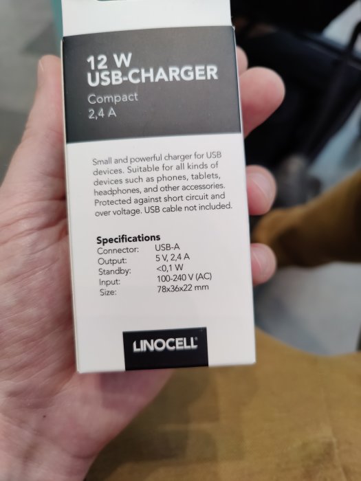 Hand som håller en Linocell 12 W USB-laddare förpackning med tekniska specifikationer synliga.