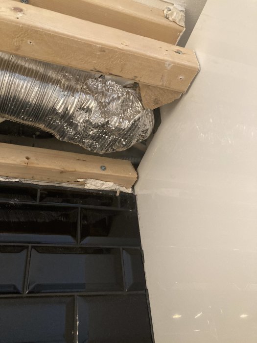 Flexibel ventilationskanal ansluten via en t-koppling nära ett tak och köksskåp, bredvid en kaklad vägg.