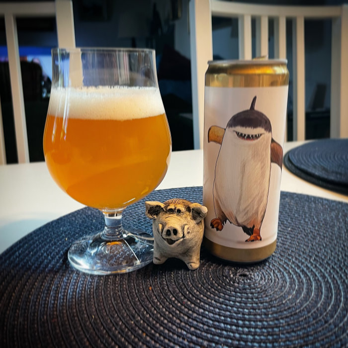 Ett glas öl bredvid en burk med illustration av en pingvin och en liten grisfigur framför på ett bord.