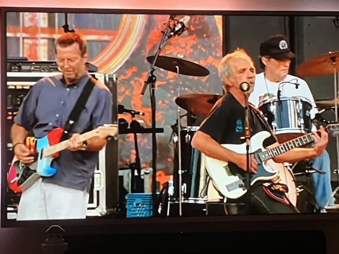 Tre män spelar musik på scen, två med gitarrer och en med trummor.