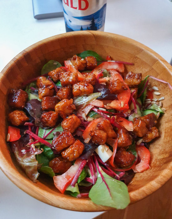 En färgrik sallad med tempeh, rostade solrosfrön och vegansk ost i en träskål.