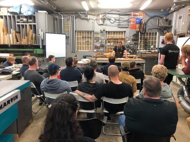 Grupp människor som deltar i en workshop i en välutrustad snickeriverkstad.