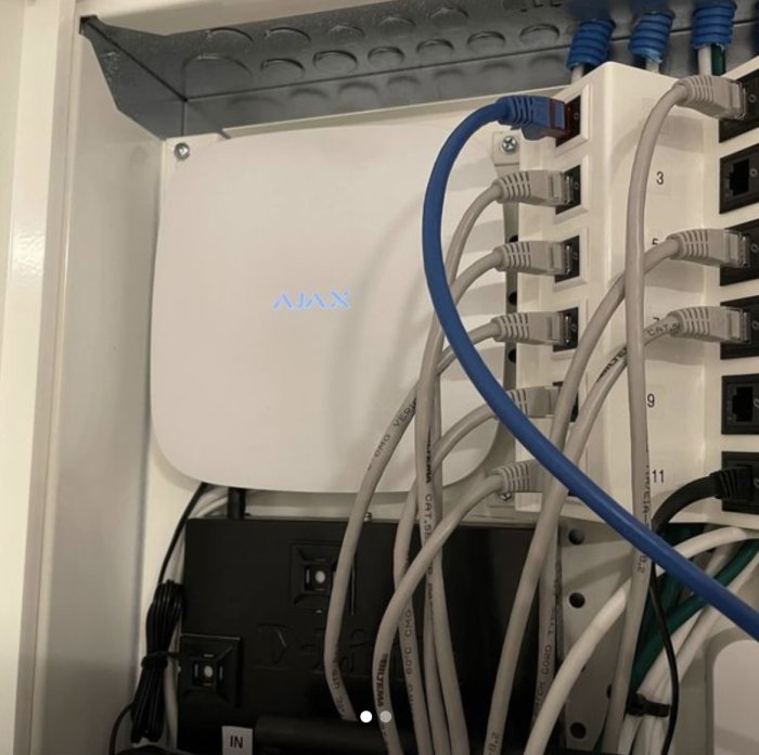 Ajax Hub säkerhetssystem monterat på vägg med nätverkskablar och patchpanel.