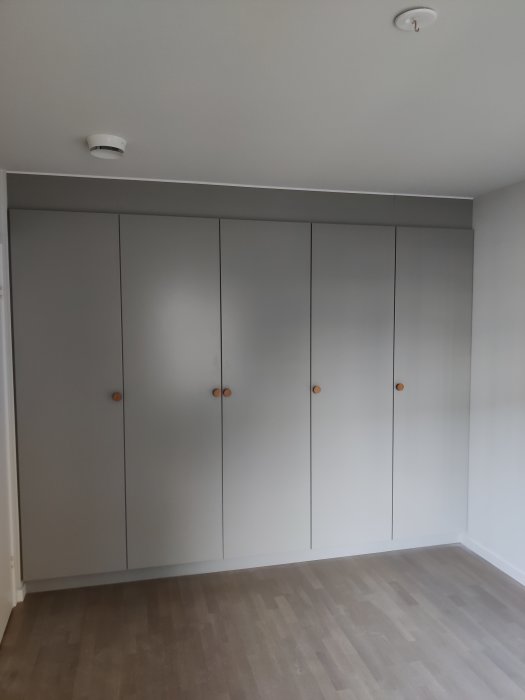Grå Ballingslöv garderober i nyproduktion med träknoppar mot ljus vägg och trägolv.