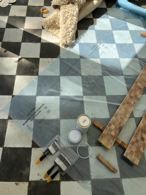 Material och verktyg för tröskelbygge med klyvda lister, epoxy, och lack på ett schackrutigt golv.