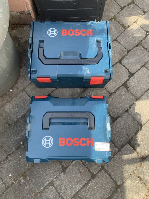 Två blå Bosch förvaringslådor i olika storlekar, den mindre framför den större, på en stenbelagd mark.