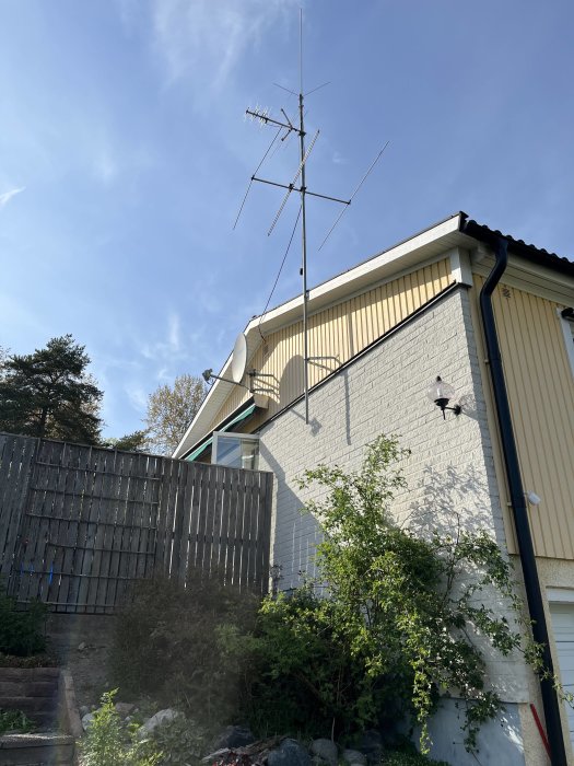 Radiomast med flera antennelement monterad på en husfasad mot en klarblå himmel.