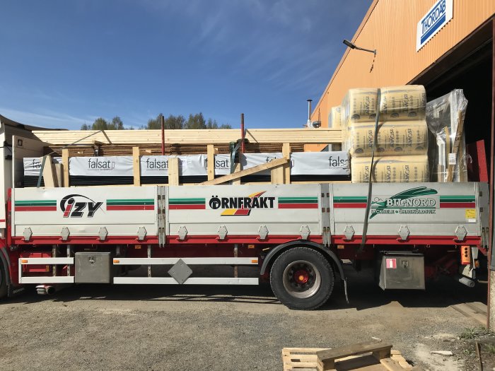 Lastbil flak fullastat med byggmaterial såsom reglar, isolering och takplåt.