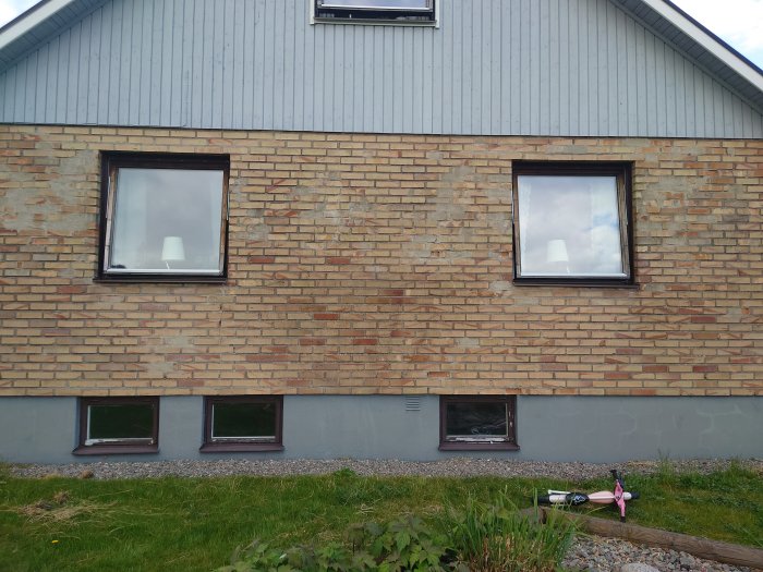 Sliten fasad av tegel från 1962 på södersidan av ett hus med synliga skador och behov av reparation.