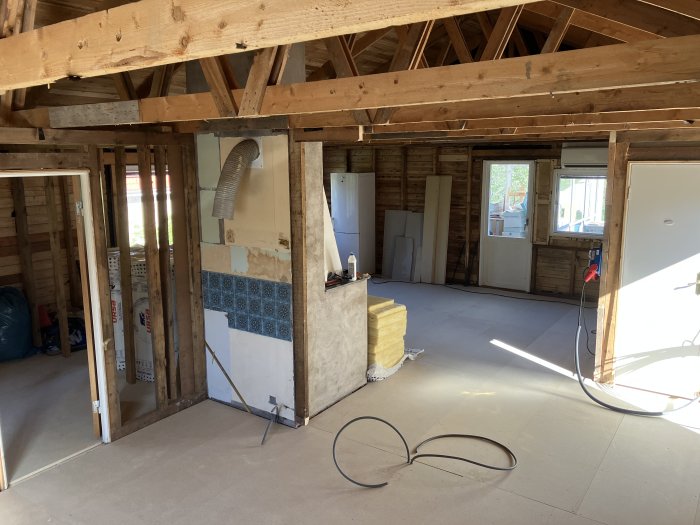 Renoveringsprojekt av ett rum med synliga träbjälkar och oavslutat golv.