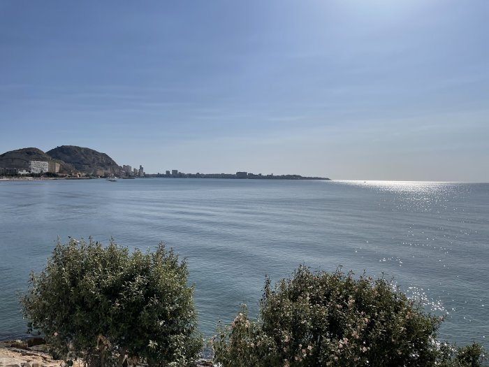 Solsken över kust och hav i Alicante med stadssilhuett i bakgrunden.