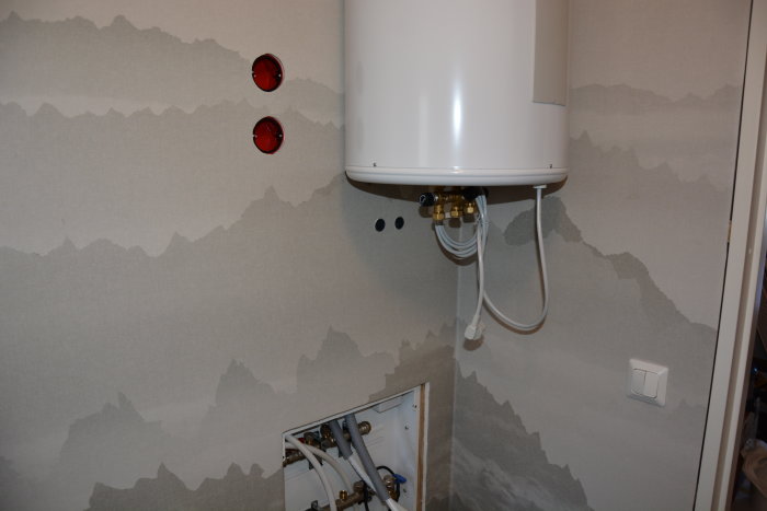 Nyinstallerad värmepanna med rördragningar på vägg med mönstrad tapet och en öppen installationslucka.