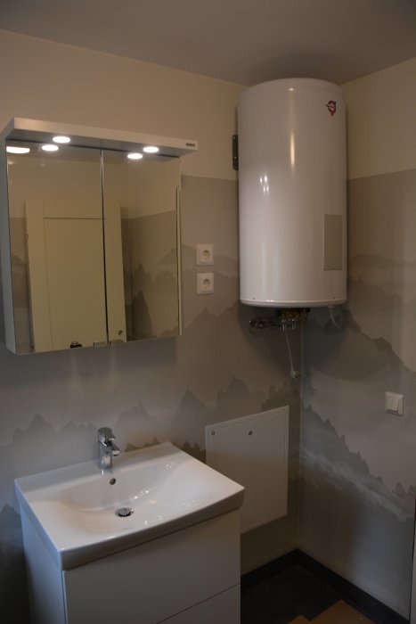 Ett nästan färdigt badrum med handfat, spegelskåp med belysning och varmvattenberedare på väggen.