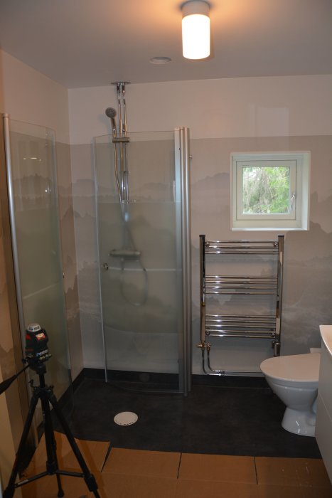 Nyrenoverat badrum med duschhörna, toalett och handdukstork, märken synliga, ej inkopplat vatten.