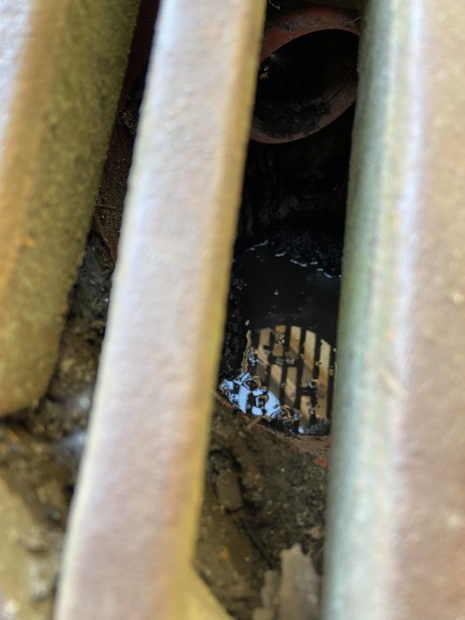 Närbild på en dagvattenbrunn med stående vatten och slam, synligt rör i bakgrunden, sett genom galleröppning.