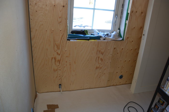 Renoveringsarbete i rum med träskivor upp till halva väggen, omonterade eluttag och material på fönsterbrädan.