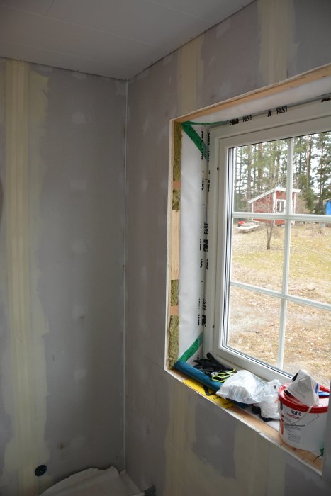 Renoveringsarbete i rum med gipsskivor och spackle på väggar, osatt fönster med utsikt.