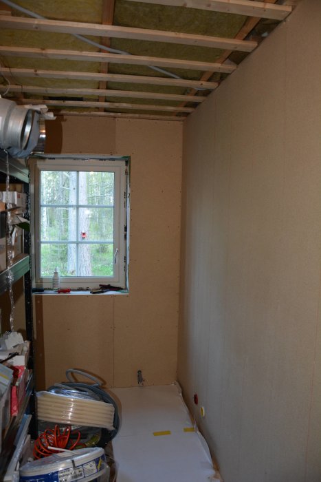 Ett pågående renoveringsprojekt av ett sovrum med halvfärdiga gipsskivor på väggen och isolering i taket.