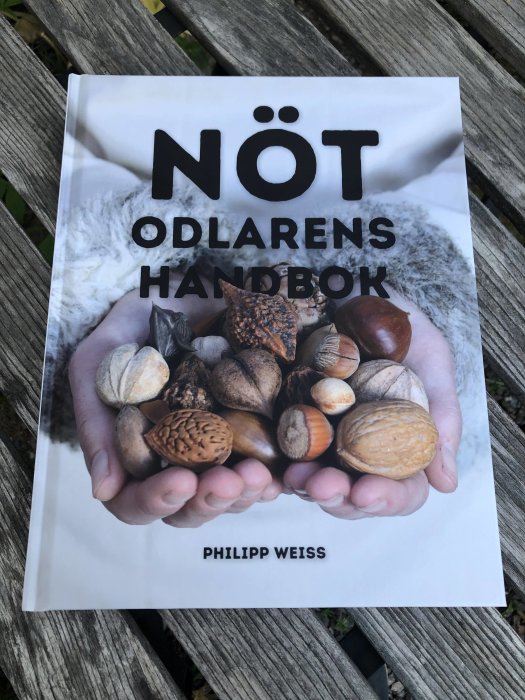 Bokomslag "Nötodlarens handbok" med händer som håller olika nötter.