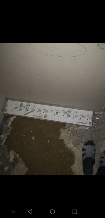 Vy från ett badrumsgolv med ett outgjutet hål och en del av en unidrain-brunn synlig, samt en persons fötter.