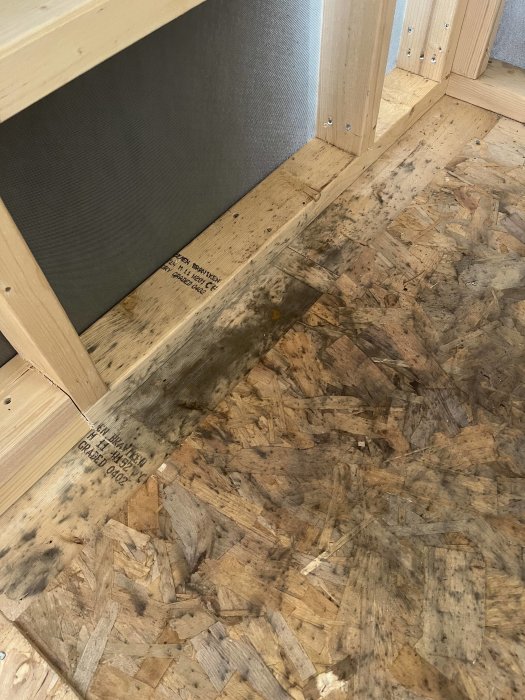 Trästomme och OSB-skiva med mörka fläckar vid byggprojekt, möjlig smuts eller mögel.