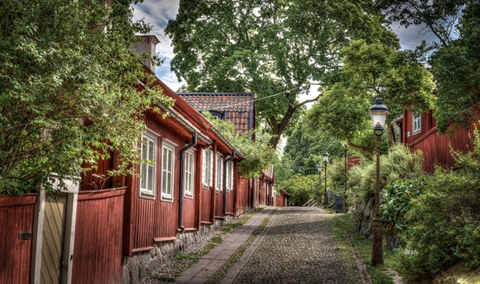 Kullerstensgata med röda trähus och plank längs med vägen i ett lugnt område.