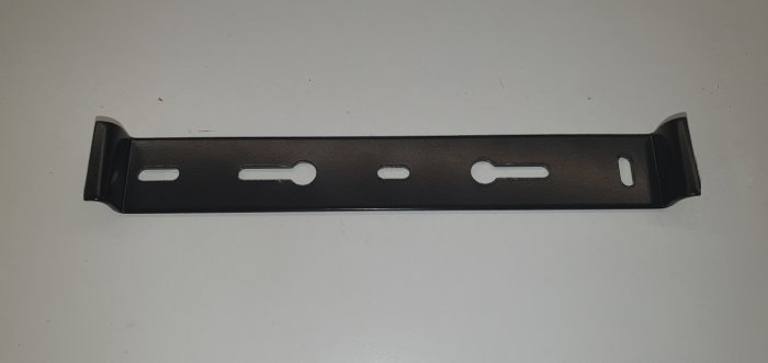 Svart metallhållare med felvända nyckelhålsfästen för takplafondinstallation.