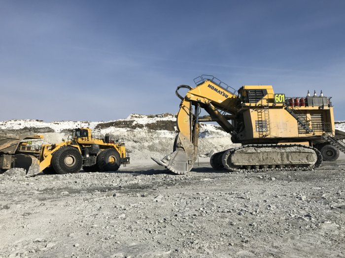 Stor grävmaskin och hjullastare i arbete i grustag med klarblå himmel i bakgrunden.