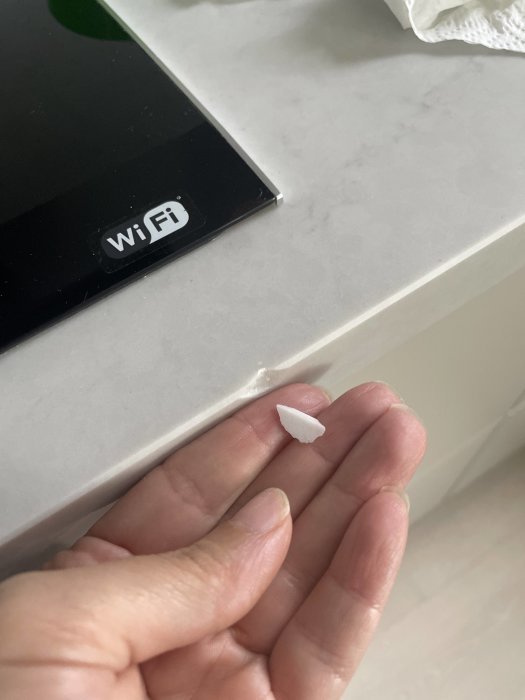 Hand håller en avbruten bit från en vit marmormönstrad bänkskiva, nära en spishäll med WiFi-symbol.