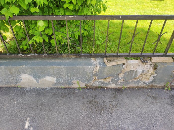 Damaged low wall with failed repair attempts and a metal fence on top.