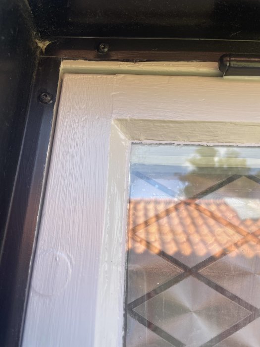 Renoverat fönster med ojämn fogning och synlig penselstruktur på träramen mot en bakgrund av takpannor.