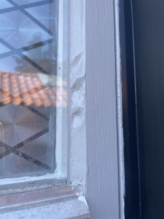 Nyligen renoverat träfönster med ojämn och klumpig omfogning längs kanterna.