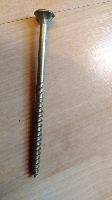 En lång skruv på 6.0x140 storlek mot en träbakgrund, avsedd för fastsättning i bjälkar.