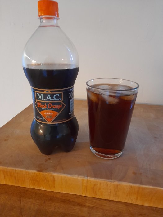 Flaska med etiketten M.A.C. Black Orange bredvid ett glas med mörk dryck och isbitar.