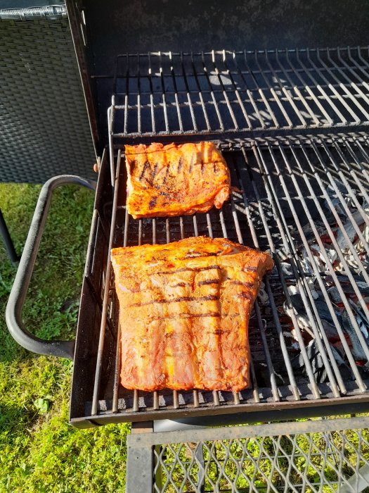 Två saftiga revbensspjäll på en grill nära färdiga, över glödande kol.