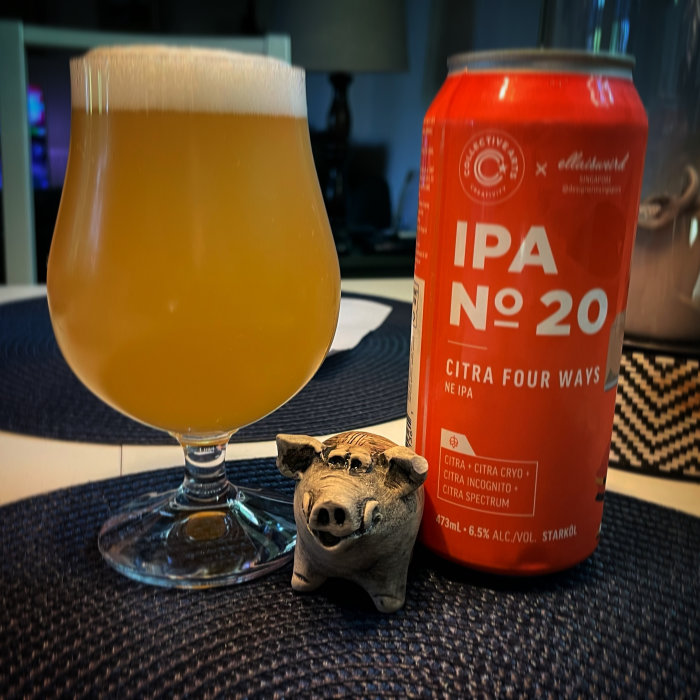 Ett ölglas fyllt med IPA bredvid en burk och en liten grisskulptur på ett bord.
