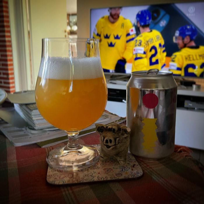 Ölglas fyllt med grumlig dryck, burk och liten grishandduk framför en TV som visar hockeymatch.