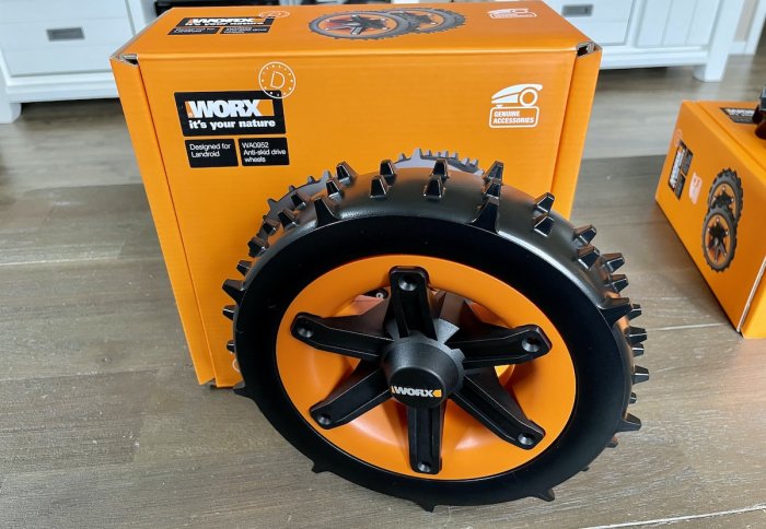 Worx allterrain-hjul med taggiga däck framför orangea förpackningar på ett golv.