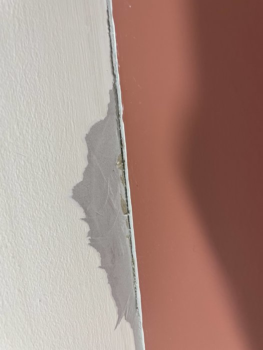 Spricka och avskalat spackel i hörnet av ett rosa och vitt målat sovrum.