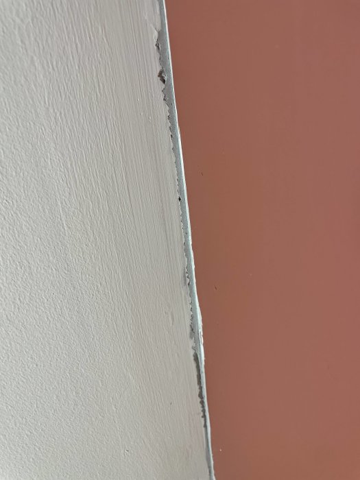 En närbild på en spricka i hörnet av ett sovrum mellan två väggar, där spackel och fog har spruckit.