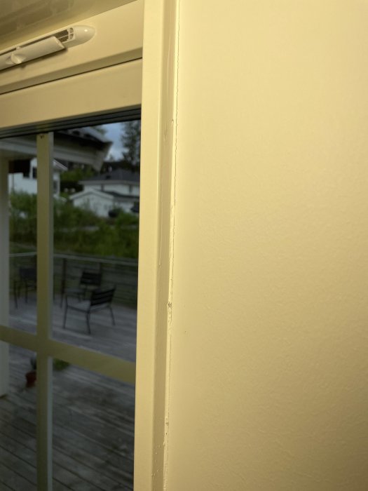 Spricka i fogen på hörnet av en gulmålad vägg med utsikt till en uteplats genom fönstret.