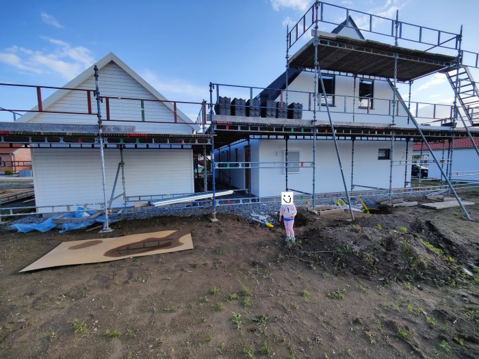 Hus och garage under renovering med synlig puts och byggställningar, person framför huset.