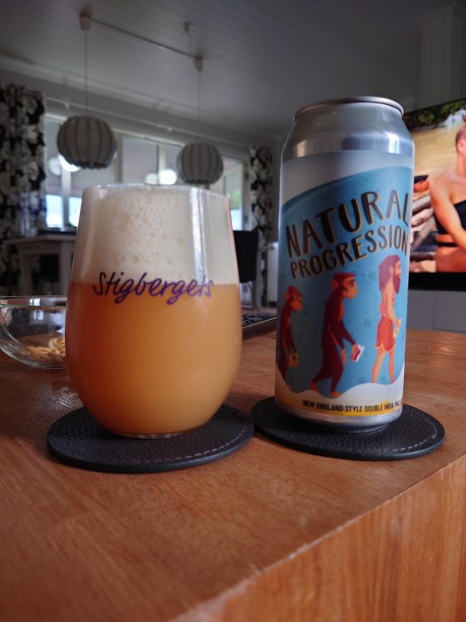 Ett ölglas fyllt med skummande dryck bredvid en burk med texten "Natural Progression" på ett träbord.