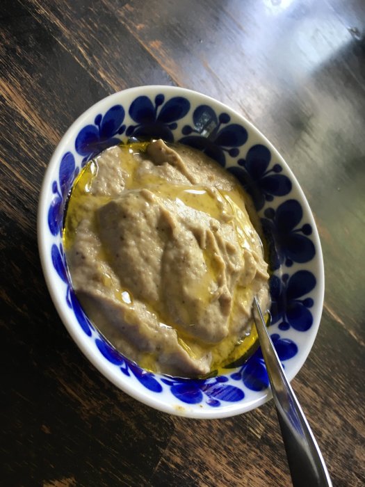 Hemlagad baba ganoush i en blåmönstrad skål med olivolja, fotograferad på ett träbord.