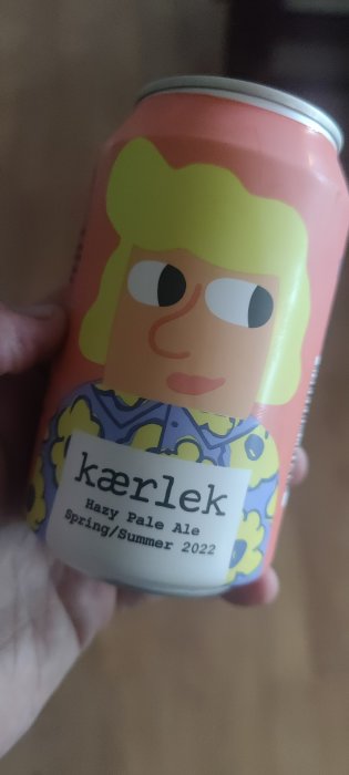 Hand håller en ölburk med färgglad karaktär, märkt 'kærlighed Hazy Pale Ale Spring/Summer 2022'.