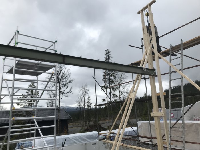 Konstruktion av byggnadsställning och pelare med utsikt över skog och molnig himmel.