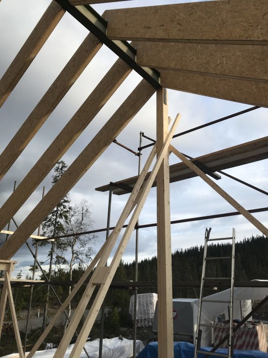 Konstruktion av trätakstolar och nockbalk uppsatt på pelare på en byggarbetsplats under klart väder.