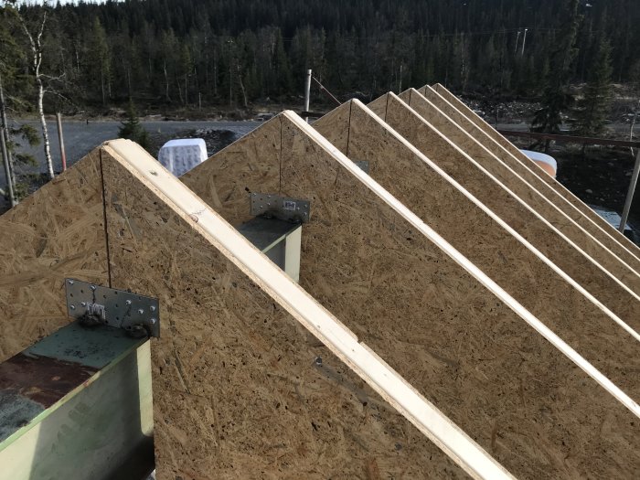 Vy över nykonstruerad takstomme med halvt uppresade takåsar på en byggarbetsplats i fint väder.